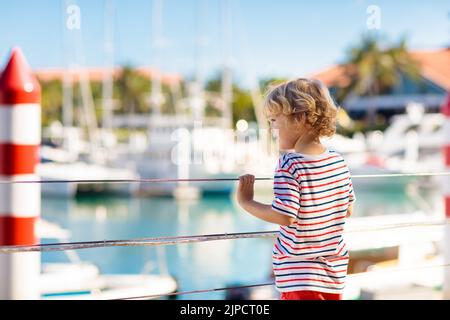 Kinderbeobachtungsyacht und Boot im Hafen. Yachtsport für Familien mit Kindern. Kleiner Junge, der in den Sommerferien in einem tropischen Resort herumläuft. Stockfoto