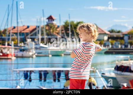 Kinderbeobachtungsyacht und Boot im Hafen. Yachtsport für Familien mit Kindern. Kleiner Junge, der in den Sommerferien in einem tropischen Resort herumläuft. Stockfoto