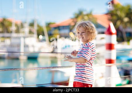 Kinderbeobachtungsyacht und Boot im Hafen. Yachtsport für Familien mit Kindern. Kleiner Junge, der in den Sommerferien in einem tropischen Resort herumläuft. Stockfoto