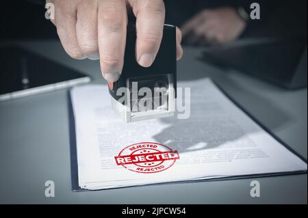 Nahaufnahme der Person Handstempel mit abgelehntem Stempel auf Dokument mit abgelehntem Text am Schreibtisch, Vertragsformularpapier. Geschäftsmann unterzeichnet Geschäftsprojekt ablehnen Stockfoto