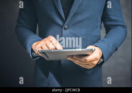 Geschäftsmann hält Tablet-Computer auf dunklem Hintergrund. Männlich Geschäftsmann Programme etwas, während hält Tablet-Computer in den Händen. Er arbeitet in Da Stockfoto