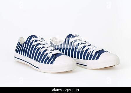 Zwei neue, trendig gestreifte, marineblau-weiße Sneakers auf weißem Hintergrund. Stockfoto