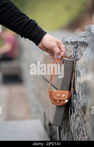 Jemand hat eine Tasche verloren. Die Hand eines Mannes nimmt eine gefundene verlorene Sache - die Handtasche der Frauen eines kleinen Kindes. Verlassene oder verlassene Gegenstände, verloren und gefunden. Stockfoto