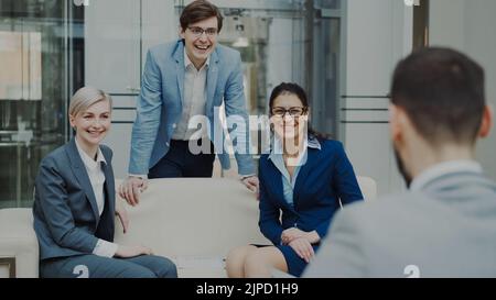 Ein Team aus fröhlichen Geschäftskollegen, die sich unterhalten und diskutieren, während sie in der modernen Bürohalle auf dem Sofa sitzen Stockfoto