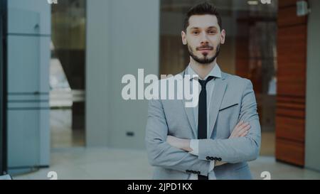 Porträt eines erfolgreichen jungen lächelnden Geschäftsmannes, der in einem modernen Büro in Innenräumen in die Kamera schaut Stockfoto
