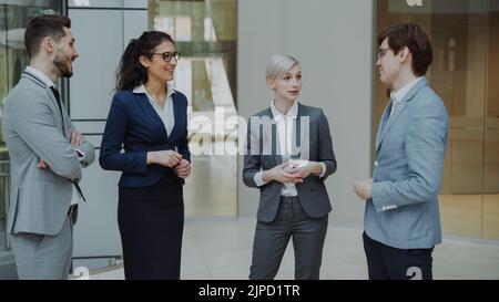 Eine Geschäftsfrau, die mit ihren Kollegen spricht, während sie in der Lobby im Büro steht. Gruppe von Geschäftsleuten, die über einen zukünftigen Deal diskutieren Stockfoto