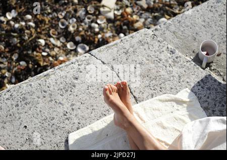 Füße Frau mit gekreuzten Beinen entspannen auf Hafenfront bei Sonnenschein auf Handtuch Stockfoto