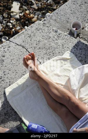 Füße Frau mit gekreuzten Beinen entspannen auf Hafenfront bei Sonnenschein auf Handtuch Stockfoto