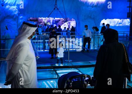 Blick auf eine arabische Familie in traditioneller Kleidung, die Schlange steht, um die Penguin Cove im Unterwasser-Zoo im Dubai Aquarium in Dubai, VAE, zu sehen Stockfoto