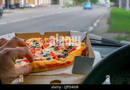 Pizza in einem Karton liegt auf einer Tafel im Inneren des Autos vor dem Hintergrund vorbeifahrenden Autos Stockfoto