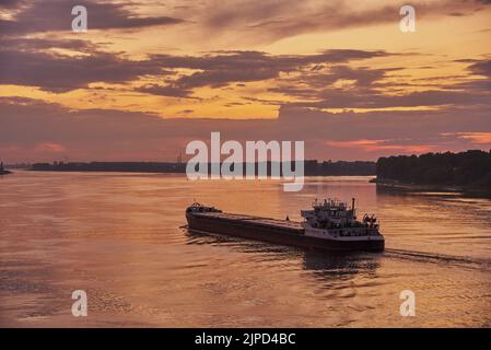 Bei Sonnenuntergang schwimmt ein Lastkahn auf dem Fluss. Sommerabendlandschaft. Stockfoto