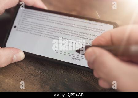 Nahaufnahme der elektronischen Signatur mit Eingabestift auf dem Smartphone-Bildschirm vor dem Hintergrund eines Holztisches Stockfoto