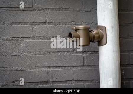 Vertikale Dachrinne an der Hausfassade mit Befestigung, die zum Verbinden des Regenfasses verwendet wird, um das Regenwasser zu sammeln Stockfoto