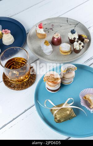 Gestapelte Makronen, umgeben von einem vereisten Whiskey-Glas und ausgefallenen Hochzeitsbonbons. Stockfoto
