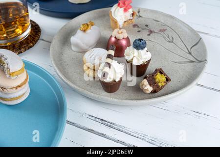 Kleiner Schokoladenbecher mit Pistazien-Cremefüllung, umgeben von verschiedenen Süßigkeiten und Whiskey-Glas. Stockfoto
