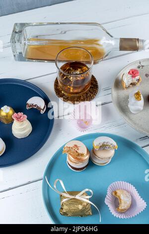 Macarons, die von Glas und einer Flasche Whiskey und Hochzeitskandys umgeben sind. Stockfoto