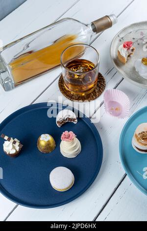 Kleiner weißer Schokoladenkuchen, umgeben von verschiedenen Hochzeitsklättchen und Whiskey-Glas. Stockfoto