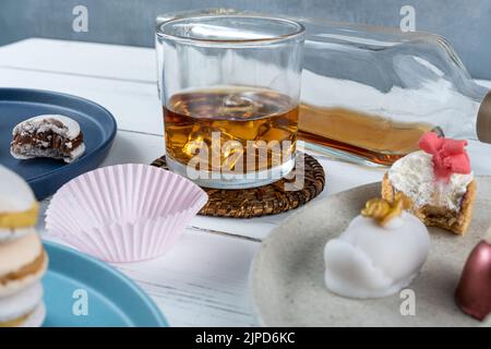 Ein Glas Whiskey mit Eis auf einer Achterbahn, umgeben von verschiedenen Hochzeitsklättchen. Stockfoto