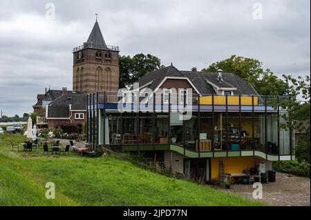 Ochten, Gelderland, Niederlande - 07 12 2022 Landhaus-Restaurant und Terrasse auf dem Deich mit dem Kirchturm im Backgorund Stockfoto