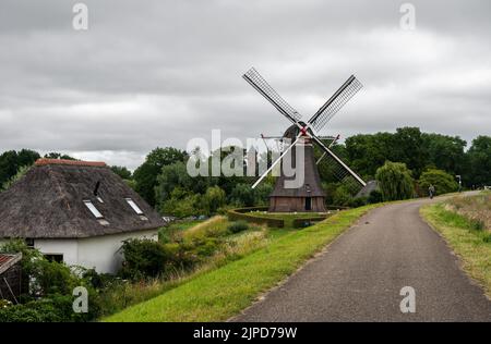 Dodewaard, Gelderland, Niederlande - 07 12 2022 - Radweg auf einem Deich mit Blick auf eine alte Windmühle Stockfoto