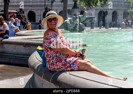 Eine Frau kühlt sich in den Fountains am Trafalgar Square ab, am heißesten Tag, den es je aufgenommen hat, London, Großbritannien Stockfoto