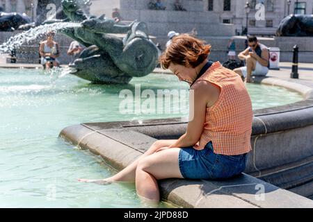 Eine junge Frau kühlt sich am heißesten Tag, den es je aufgenommen hat, in den Fountains am Trafalgar Square ab, London, Großbritannien Stockfoto