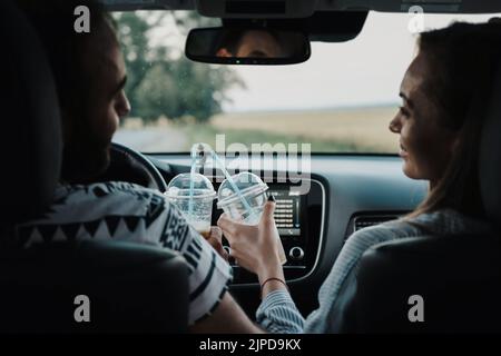 Rückansicht auf ein Paar mittleren Alters, das im Auto sitzt und Kaffee trinkt, Mann und Frau genießen gemeinsam die Autoreise Stockfoto