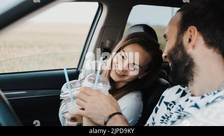Kaukasische fröhliche Frau sitzt im Auto und trinkt Kaffee mit ihrem Freund, glückliches Paar mittleren Alters auf Reise Stockfoto