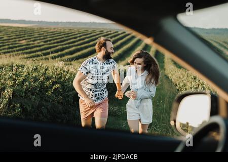 Blick durch das Autofenster, glückliches Paar mittleren Alters, das auf den wunderschönen Feldern läuft, kaukasischer Mann und Frau, die ihren Urlaub im Freien genießen Stockfoto