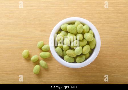 Schüssel mit Wasabi Erdnüsse auf Tabelle, die einige Muttern aus der Schüssel schoss aus direkt über verstreut sind beschichtet Stockfoto