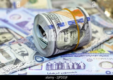 American Money roll with a Band on a pile of American Dollar Geldscheine American Cash Money Banknoten mit Saudi-Arabien riyals Geldscheine und New Emir Stockfoto