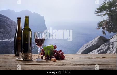 Bild von zwei Flaschen und einem Glas Wein, die am frühen Morgen auf einem Holztisch über dem Berghintergrund stehen Stockfoto