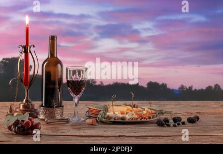 Flasche köstlicher Rotwein, Snacks, Vorspeisen mit Käse und Honig, Oliven und Trauben. Romantischer Abend mit Kerzen. Sonnenuntergang Naturlandschaft Stockfoto