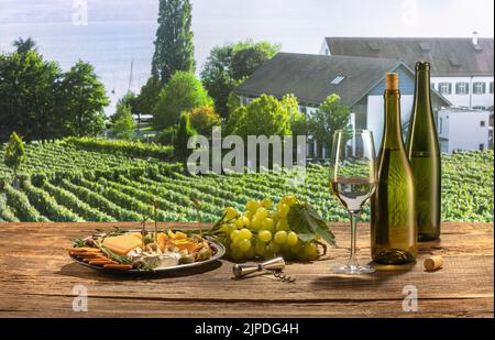 Zwei Flaschen und ein Glas köstlicher Weißwein stehen auf einem Holztisch. Leckere Vorspeisen mit Käse, Honig, Trauben und Crackern. Sommerweingarten Stockfoto