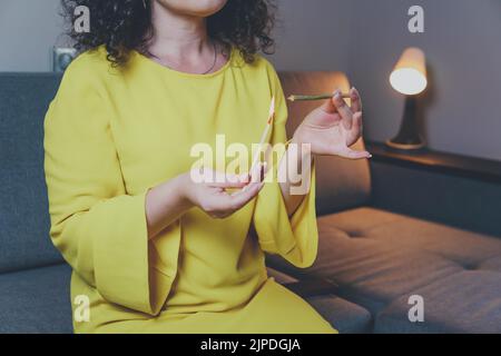 Die Nahaufnahme einer erwachsenen Frau leuchtet mit Streichhölzern und rauchenden medizinischen Marihuana-Gelenken auf. Konzept der pflanzlichen und alternativen Medizin Stockfoto