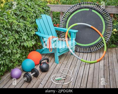 Home Fitness- und Erholungskonzept - Slam-Kugeln, Eisen-Kettlebell, Hantel, Mini-Trampolin, Widerstandsband, Springseil, und Hula Hoop Reifen mit Adirondack ch Stockfoto