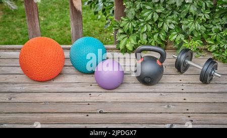 Drei schwere Slam-Kugeln, Eisen-Kugelhantel und Hantel auf einem Hinterhof-Deck, Heim- und Hinterhof-Fitnessstudio-Konzept Stockfoto