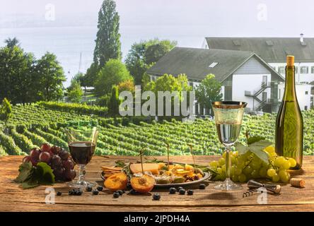 Köstlicher Weiß- und Rotwein, der auf einem Holztisch steht. Leckeres und romantisches Frühstück. Vorspeisen mit Käse, Honig, Trauben, Früchten und Crackern Stockfoto