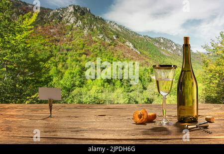 Sommerurlaub. Dunkle Flasche weißen trockenen Wein in Glas gegossen, auf Holztisch isoliert über Berglandschaft. Stockfoto