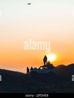 Eine Gruppe von Redakteuren von Reisenden steht im Naturabenteuer an 4WD Fahrzeugen zusammen und beobachtet den Sonnenuntergang über dem Horizont über der Wolkenlandschaft in der Wildnis Stockfoto