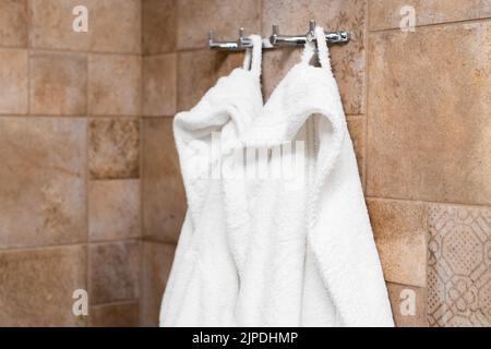 Frische weiße Bademäntel hängen an Haken im Badezimmer im Hotelzimmer Stockfoto