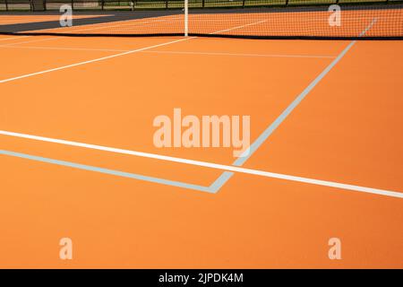 Ungewöhnlicher orangefarbener Outdoor-Tennisplatz mit weißen Linien und kombinierten hellgrauen Pickleball-Linien. Stockfoto