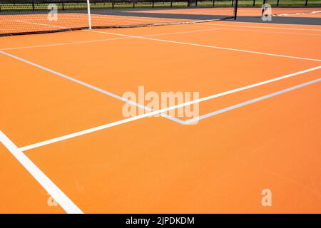 Ungewöhnlicher orangefarbener Outdoor-Tennisplatz mit weißen Linien und kombinierten hellgrauen Pickleball-Linien. Stockfoto