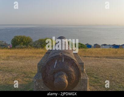 Alte Rusty Kanone auf dem Hügel mit Blick auf den Strand und die Strandhütten Whitstable Stockfoto