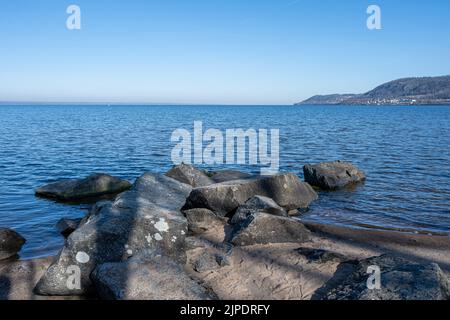 Felsbrocken als Teil eines Wellenbrechers in einem See. Bild vom See Vattern, Schweden. Blaues Wasser und Himmel im Hintergrund Stockfoto