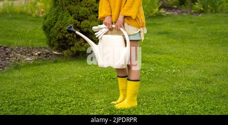 Eine professionelle Gärtnerin mit einer Gießkanne bewässert ihren Rasen und ihre Blumen. Stockfoto