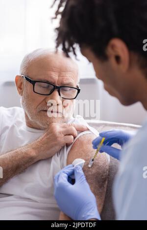 afroamerikanische Krankenschwester, die Baumwollkissen hält und ältere Patienten zu Hause injiziert Stockfoto