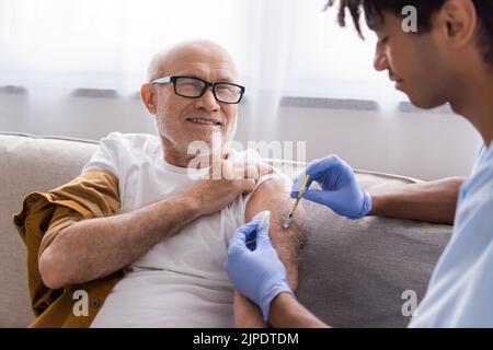 afroamerikanische Krankenschwester, die zu Hause lächelnden älteren Mannes Injektionen verabreicht Stockfoto