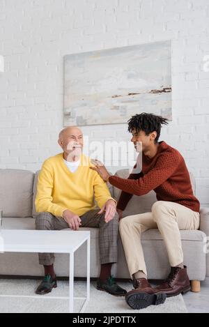 Glücklicher afroamerikanischer Enkel, der zu Hause Großeltern auf der Couch umarmt Stockfoto