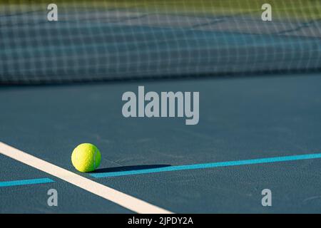 Gelber Tennisball auf einem neuen blauen Tennisplatz mit hellblauen Pickleball-Linien. Stockfoto